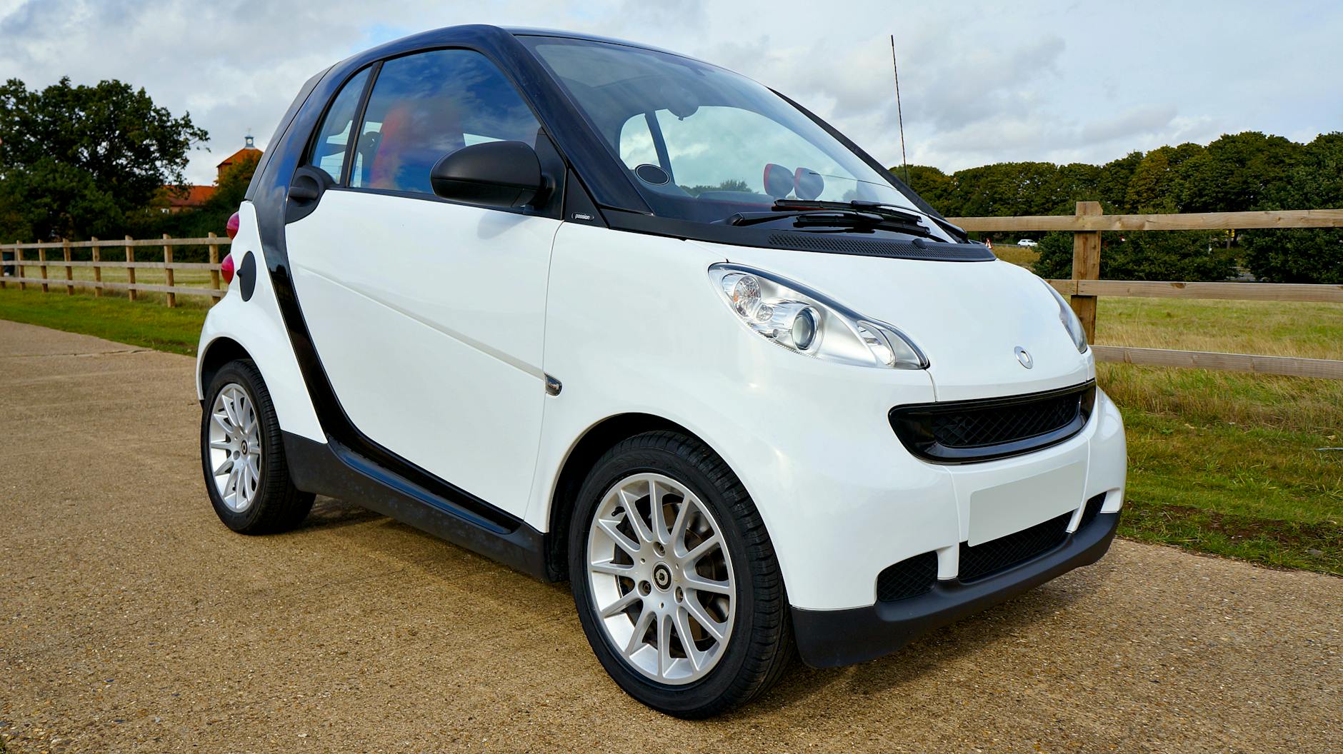 Biały samochód Smart Fortwo zaparkowany na tle zieleni i błękitnego nieba Biały samochód Smart Fortwo zaparkowany na tle zieleni i błękitnego nieba